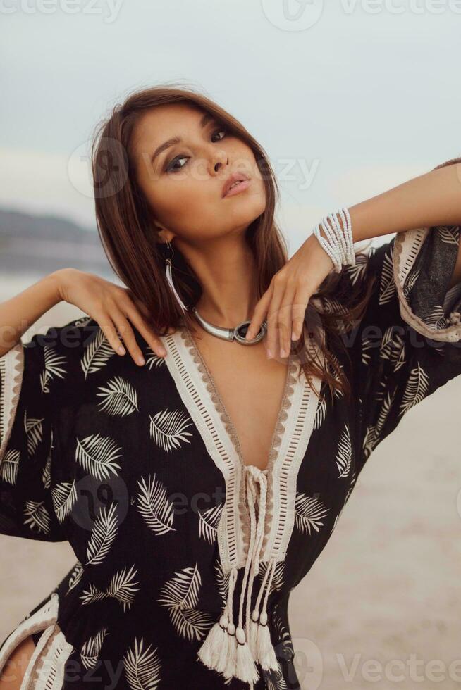 Close up portrait of  beautiful Asian woman in bohemian dress, ethnic jewelry and earring with feathers posing on the beach. photo