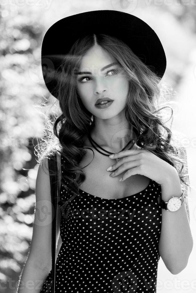 Summer fashion  portrait of r elegant woman with  perfect wavy  hair   in  stylish elegant black hat and bright make up posing in the park.  Street style. photo