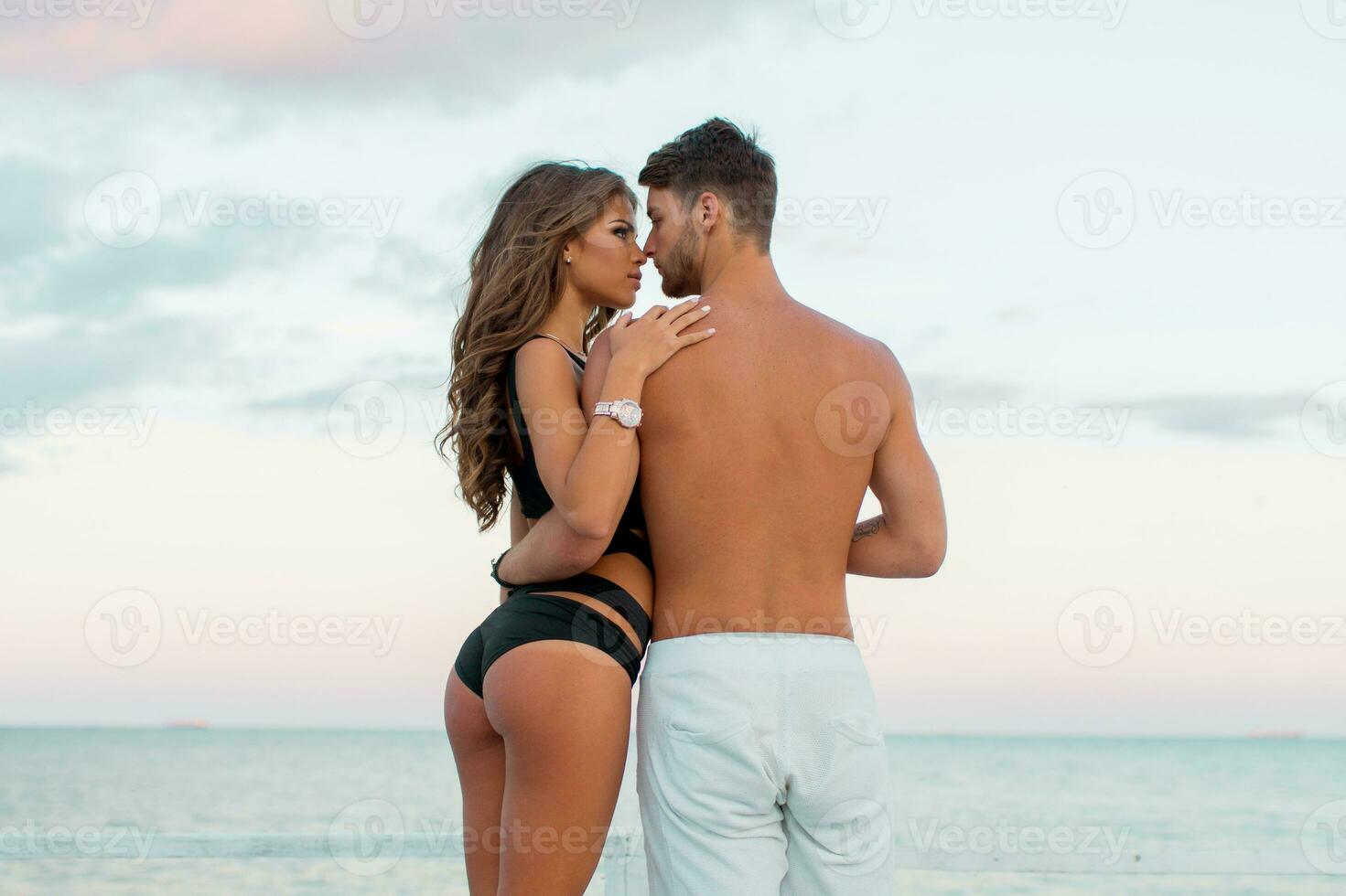 Outdoor close up fashion portrait of pretty sexy couple in love  hugs on  amazing tropical  beach, wearing stylish swimwear. photo