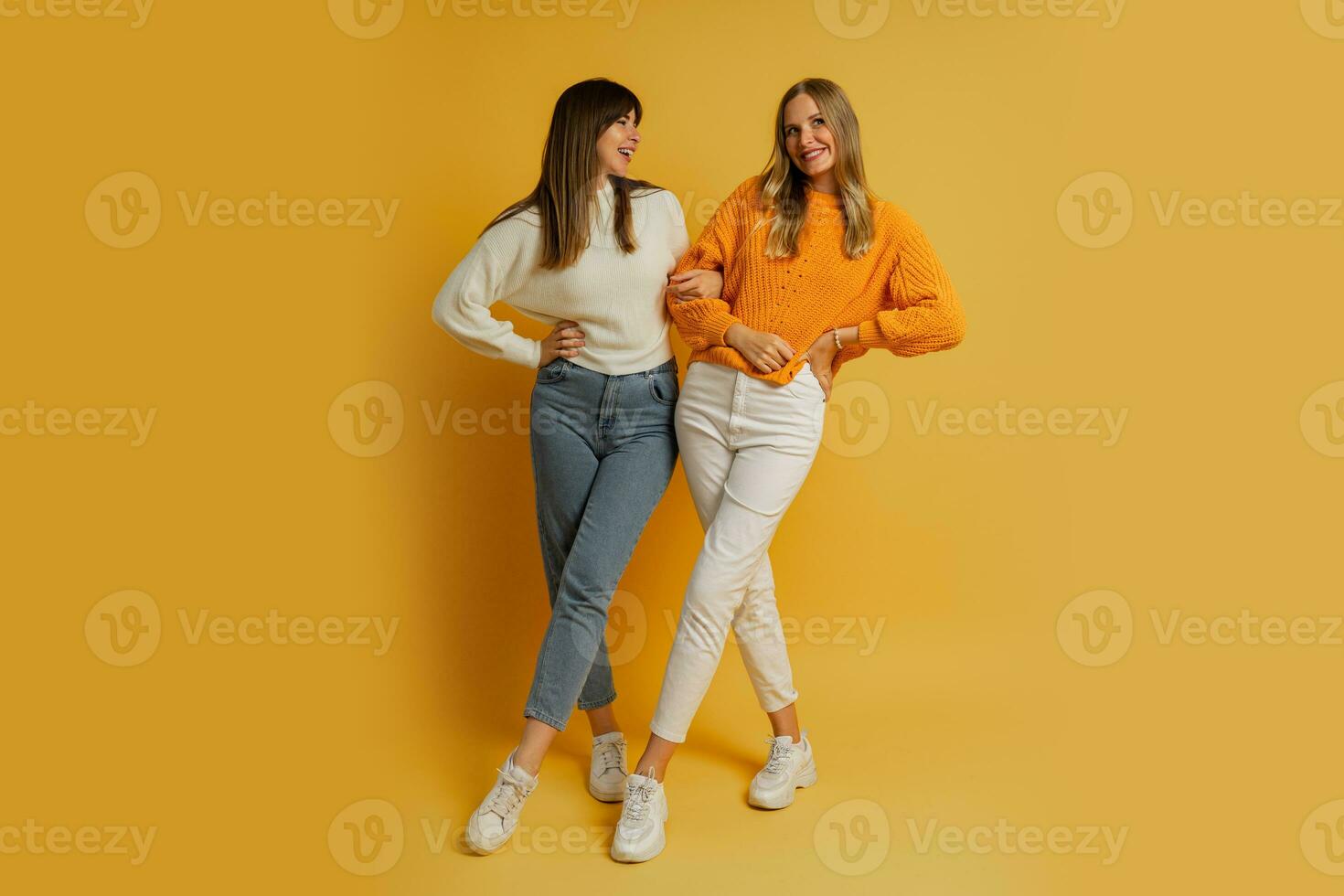 Two pretty women , best friends in stylish autumn  casual clothes having fun  over yellow background in studio. Full lenght. photo