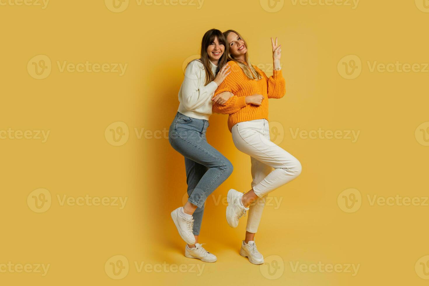 Two pretty women , best friends in stylish autumn  casual clothes having fun  over yellow background in studio. Full lenght. photo