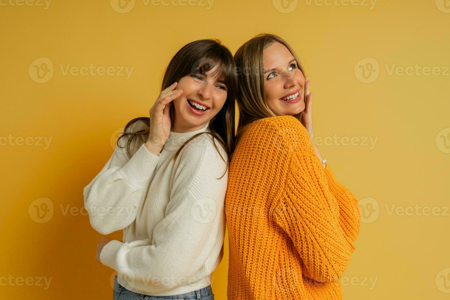cerca arriba retrato de dos bonito mujer en acogedor suéteres posando terminado amarillo antecedentes. otoño y invierno Moda tendencias foto
