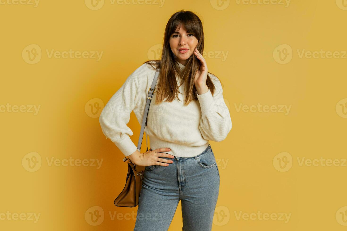 Elegant woman posing in studio on yellow background. Wearing  white wool sweater and jeans. photo