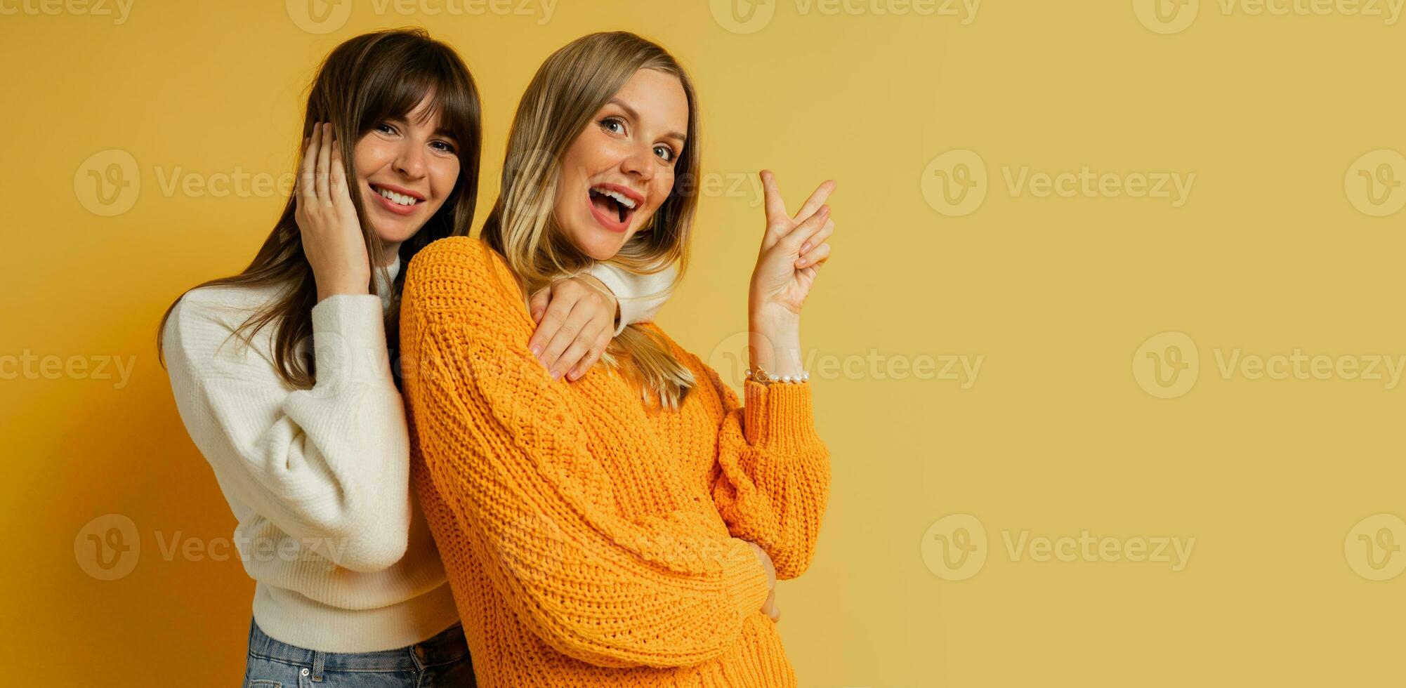 Close up portrait  of two pretty woman in cozy sweaters posing over yellow background.  Autumn and winter fashion trends. photo