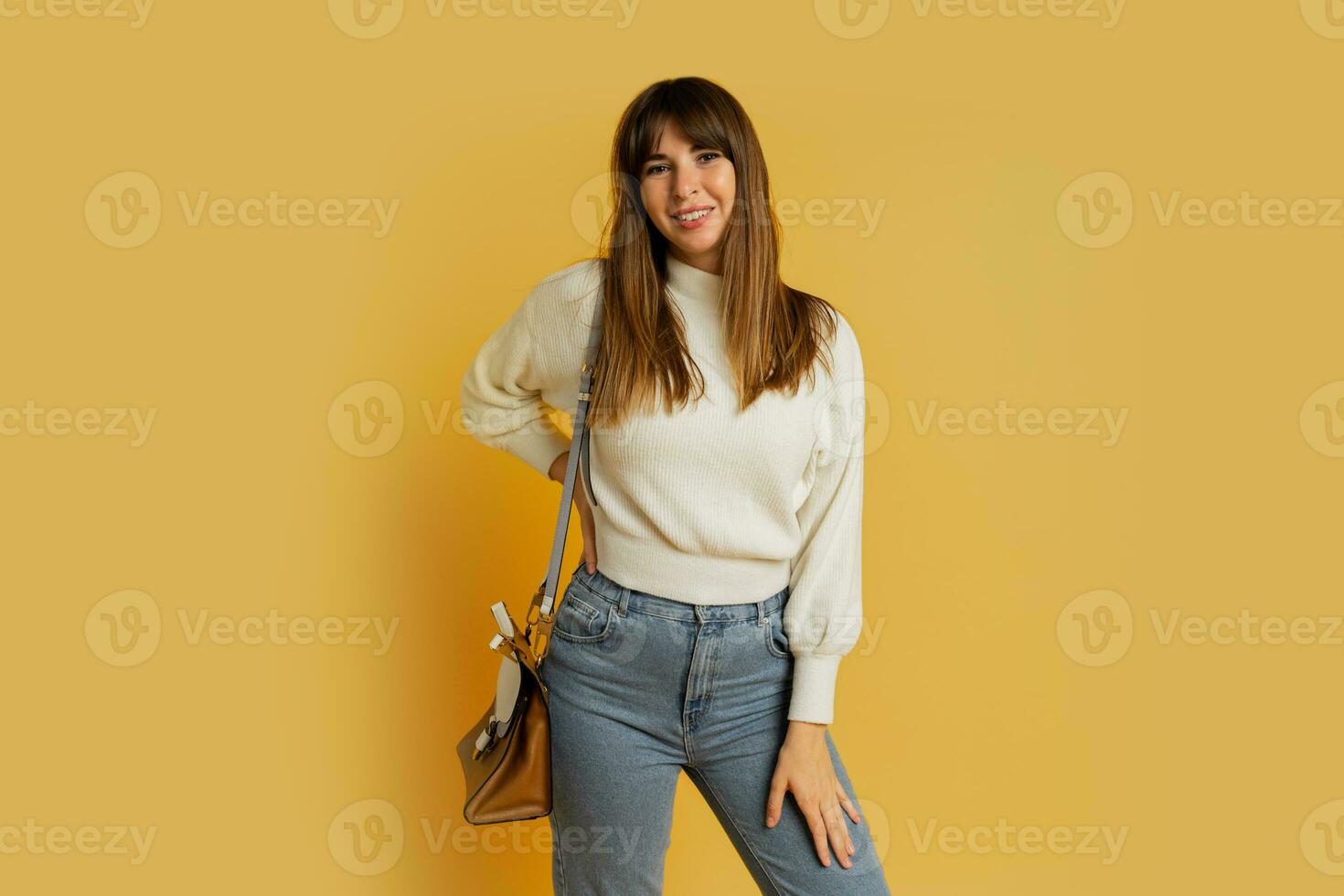 Elegant woman posing in studio on yellow background. Wearing  white wool sweater and jeans. photo