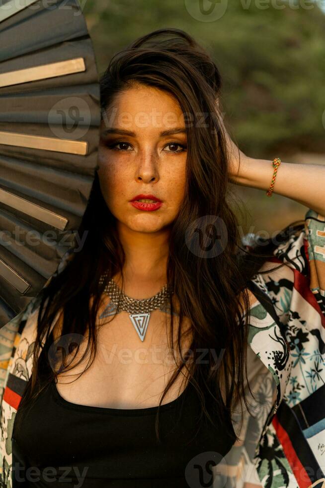 Close up portrait of seductive japanese girl in stylish  kimono  with large fan and professional make up posing on the beach. photo