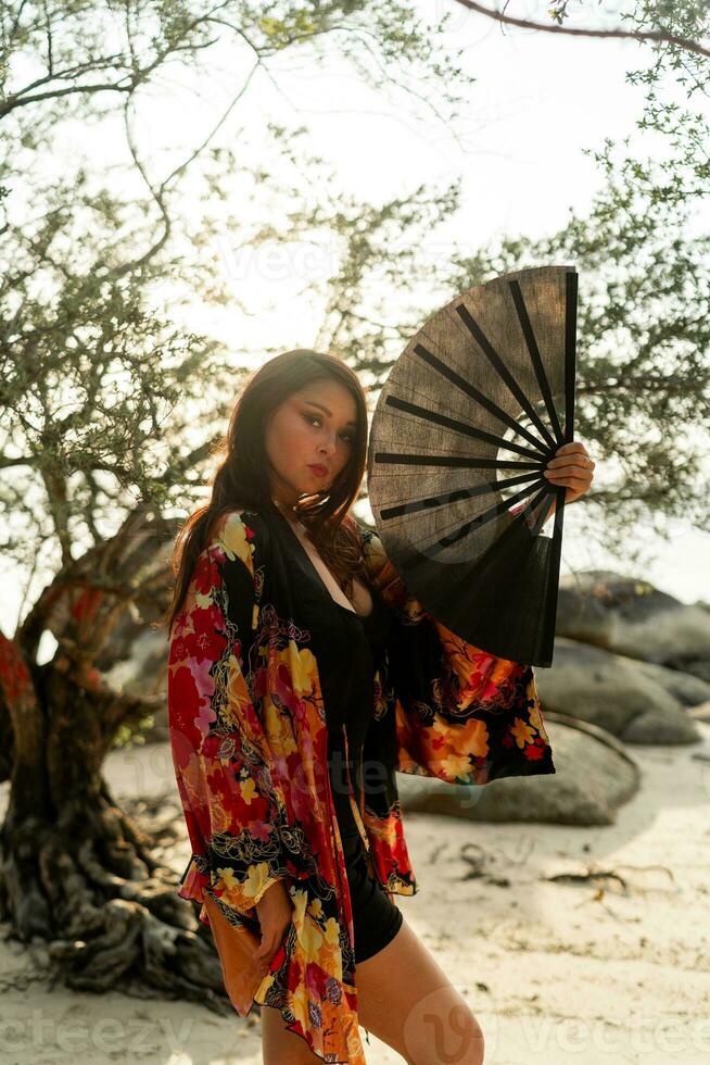 elegante mujer en elegante kimono con grande ventilador y profesional hacer arriba posando exterior. foto