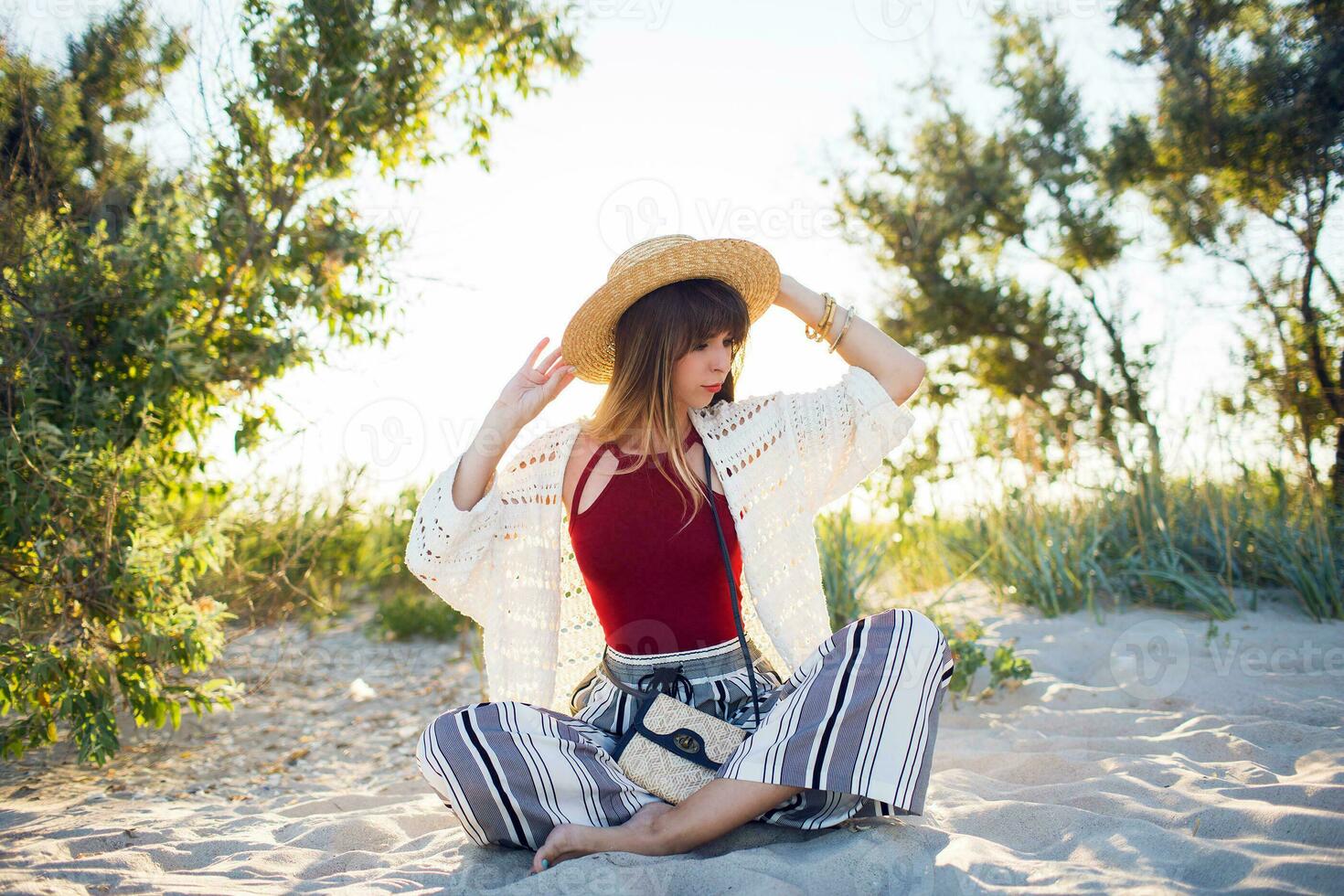 Outdoor summer photo of pretty woman in straw hat posinf on the beach at sunset light.