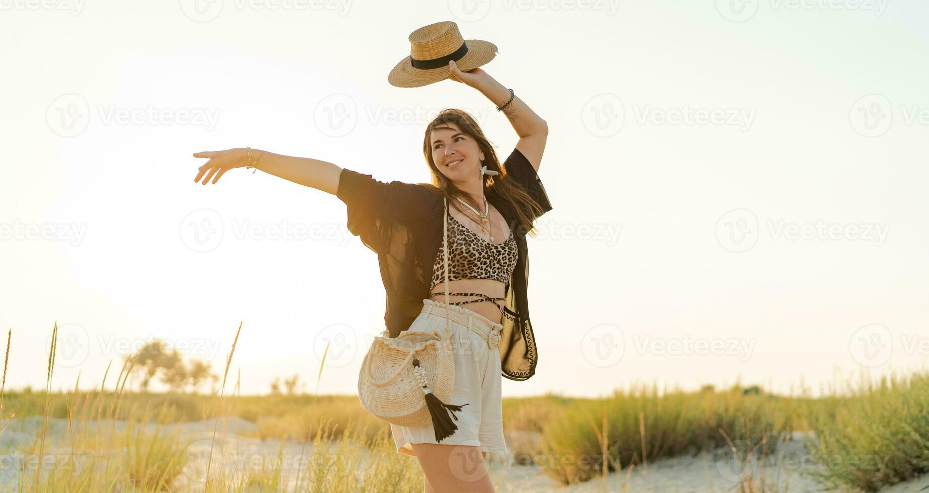 verano foto de contento joven mujer en elegante boho atuendo participación Paja bolso y sombrero posando en el l playa. lleno largo.