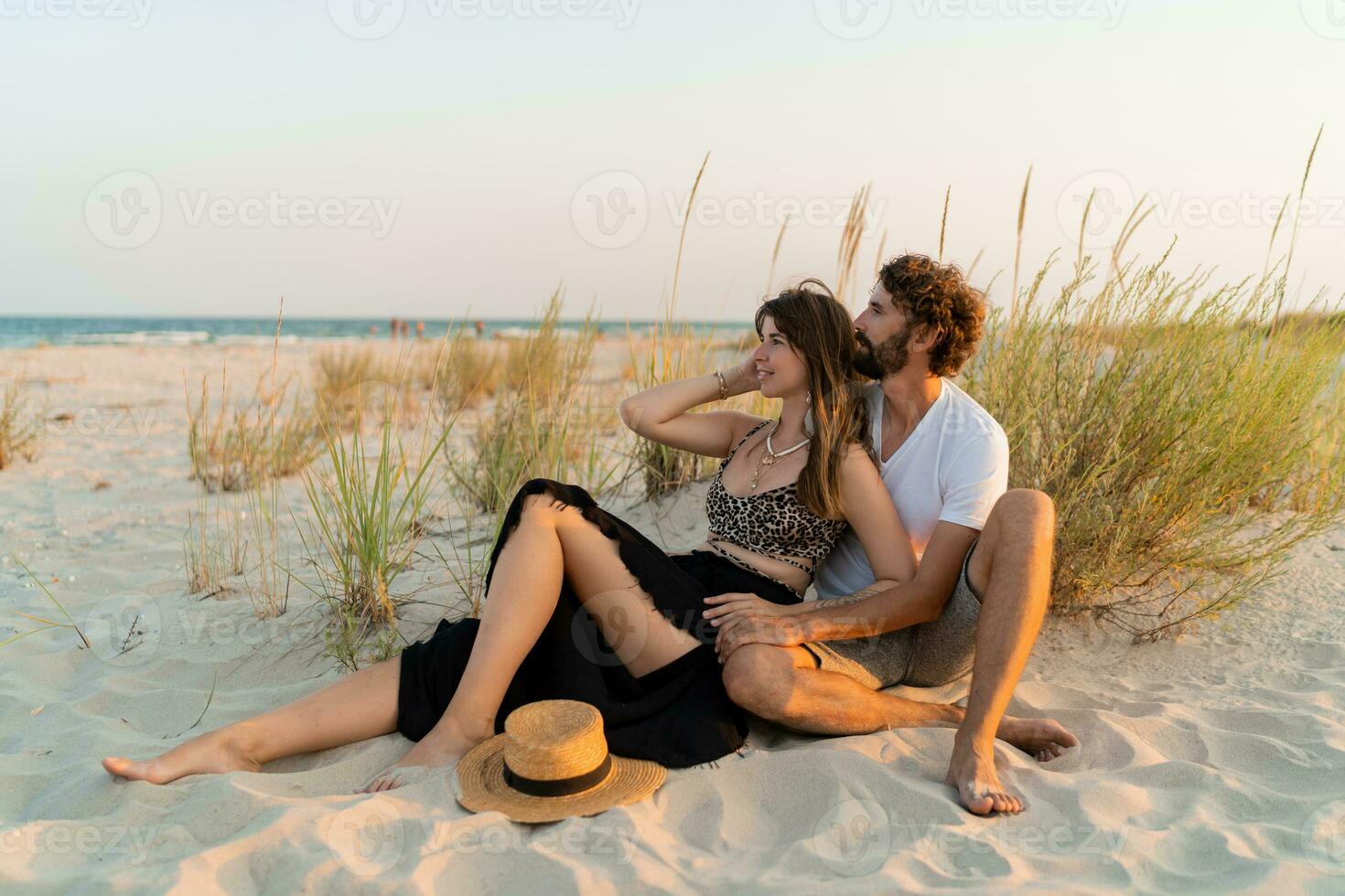 Stylish couple in love posing on the beach. Brunette woman in straw hat with her  boyfriend chilling in warm summer evening. photo