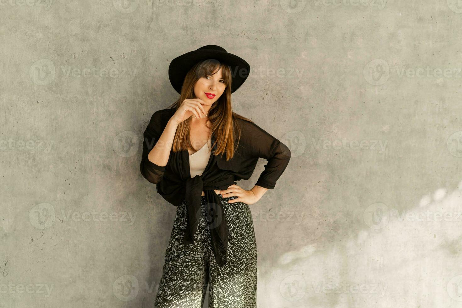 elegante europeo mujer con rojo labios en casual elegante otoño autfit. posando terminado gris urbano pared. vistiendo negro sombrero. foto