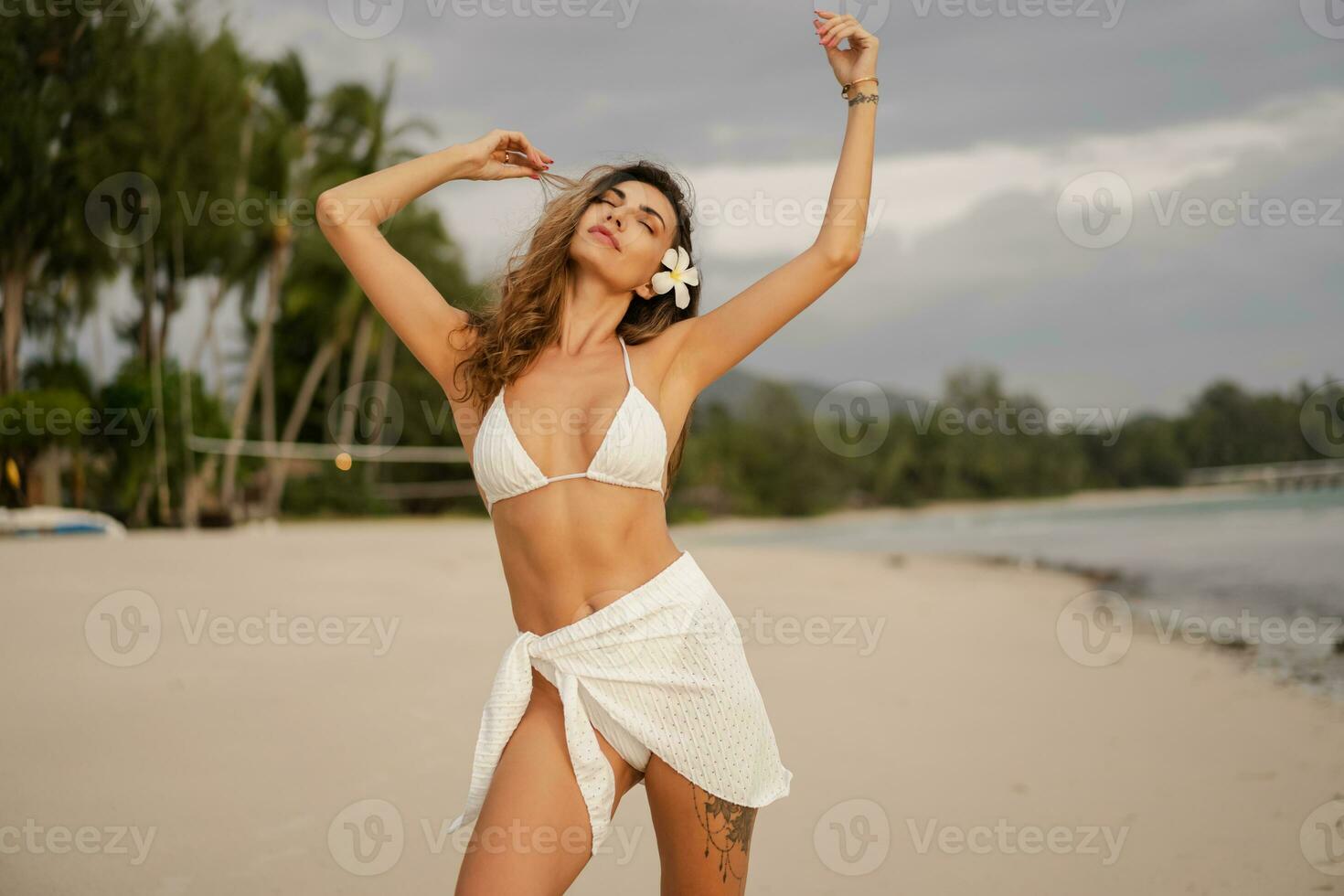 Beautiful  woman with wavy hairs  in sexy swimwear posing on the beach in sunset light. Tan slim body. Summer tropical mood. photo