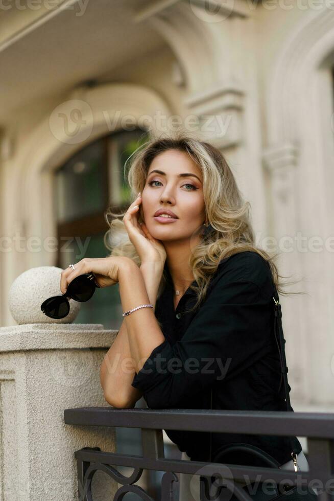 Outdoor portrait of beautiful  blond woman   with perfect make up and  wavy hairs  looking at camera.  Fashion acsessories , Casual outfit. photo