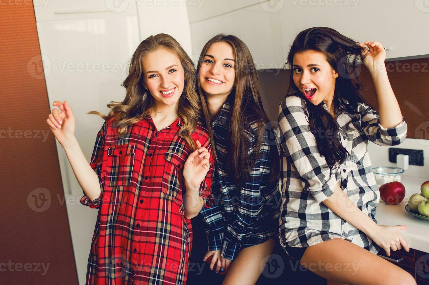 cerca arriba interior estilo de vida retrato de Tres gracioso joven amigos tener divertido y fingiendo caras en el cocina . hogar fiesta humor. vistiendo tartán camisa. calentar suave foto. foto