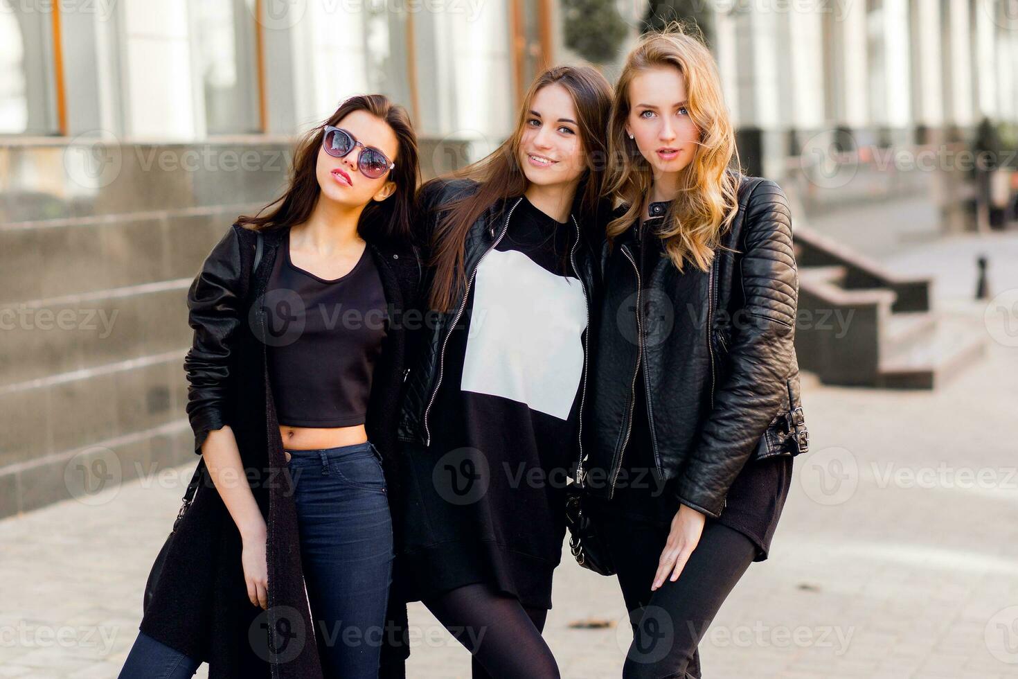 Three pretty  young girls having fun outdoors together . Lifestyle urban mood.  Center city background. Best friends wearing black casual outfit. photo