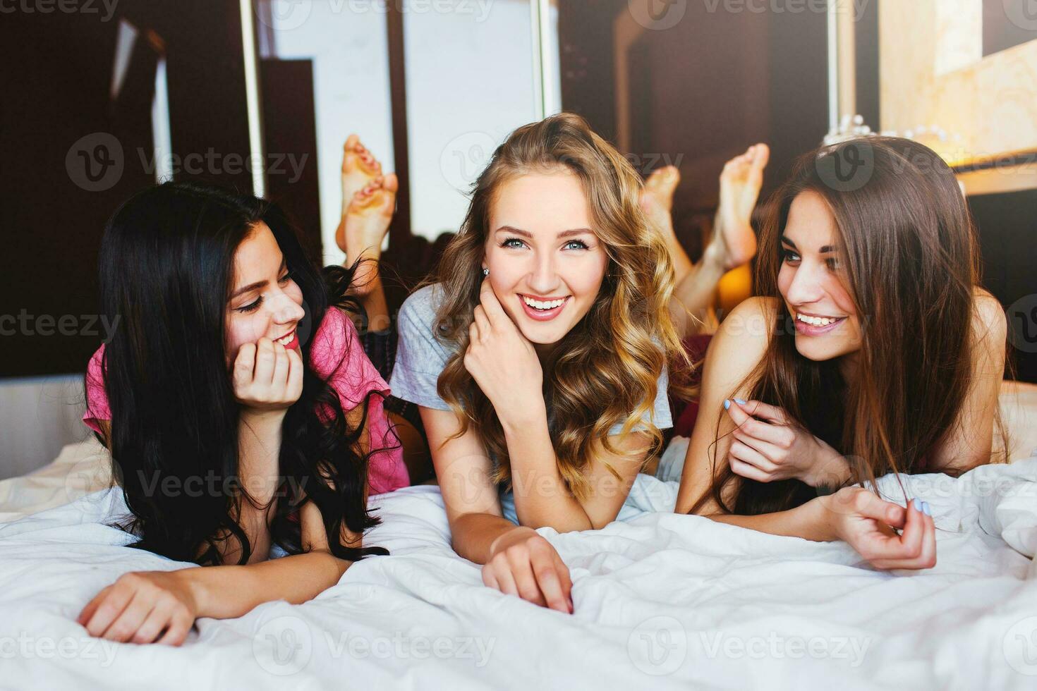 friends tell secrets in  bed . Group of pretty  young  women  in pajamas.  Sunny warm colors. Cozy atmosphere. photo