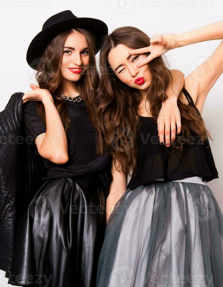 Moda retrato de dos elegante elegante mujer vistiendo un cuero falda y negro sombrero. posando en contra blanco antecedentes.ellos sonriente y mirando a cámara. foto