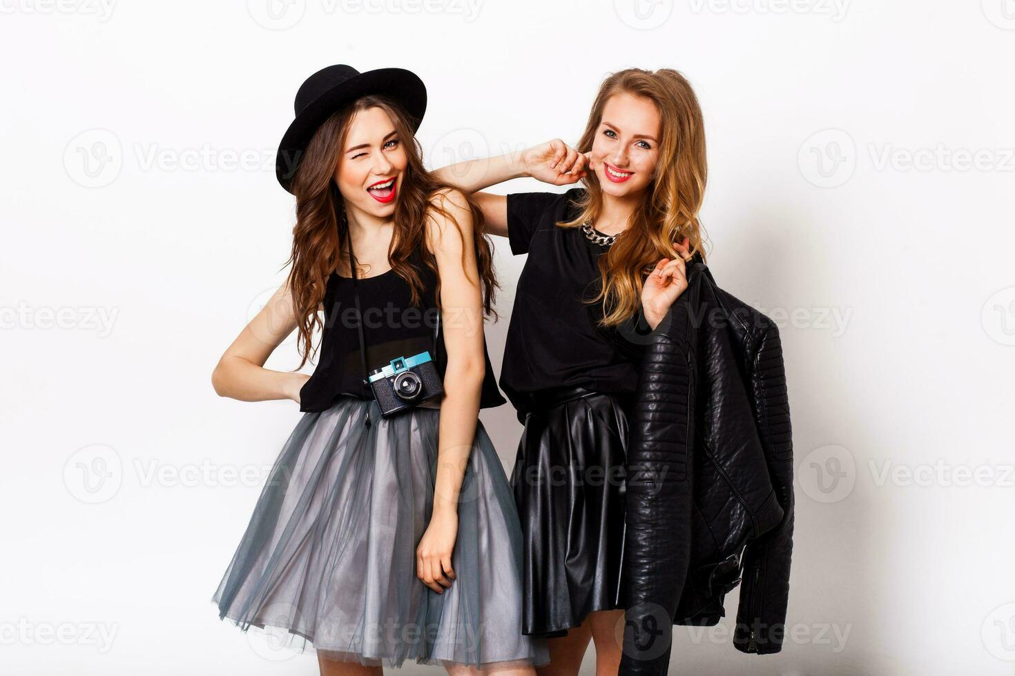 fashion portrait of two elegant stylish  women wearing a leather  skirt and black hat , holding  retro camera.  Posing against white background. photo