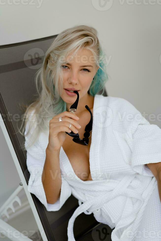 Beautiful blond woman in white robe chilling  on deck chair in luxury hotel. Perfect skin,  beautiful eyes. photo