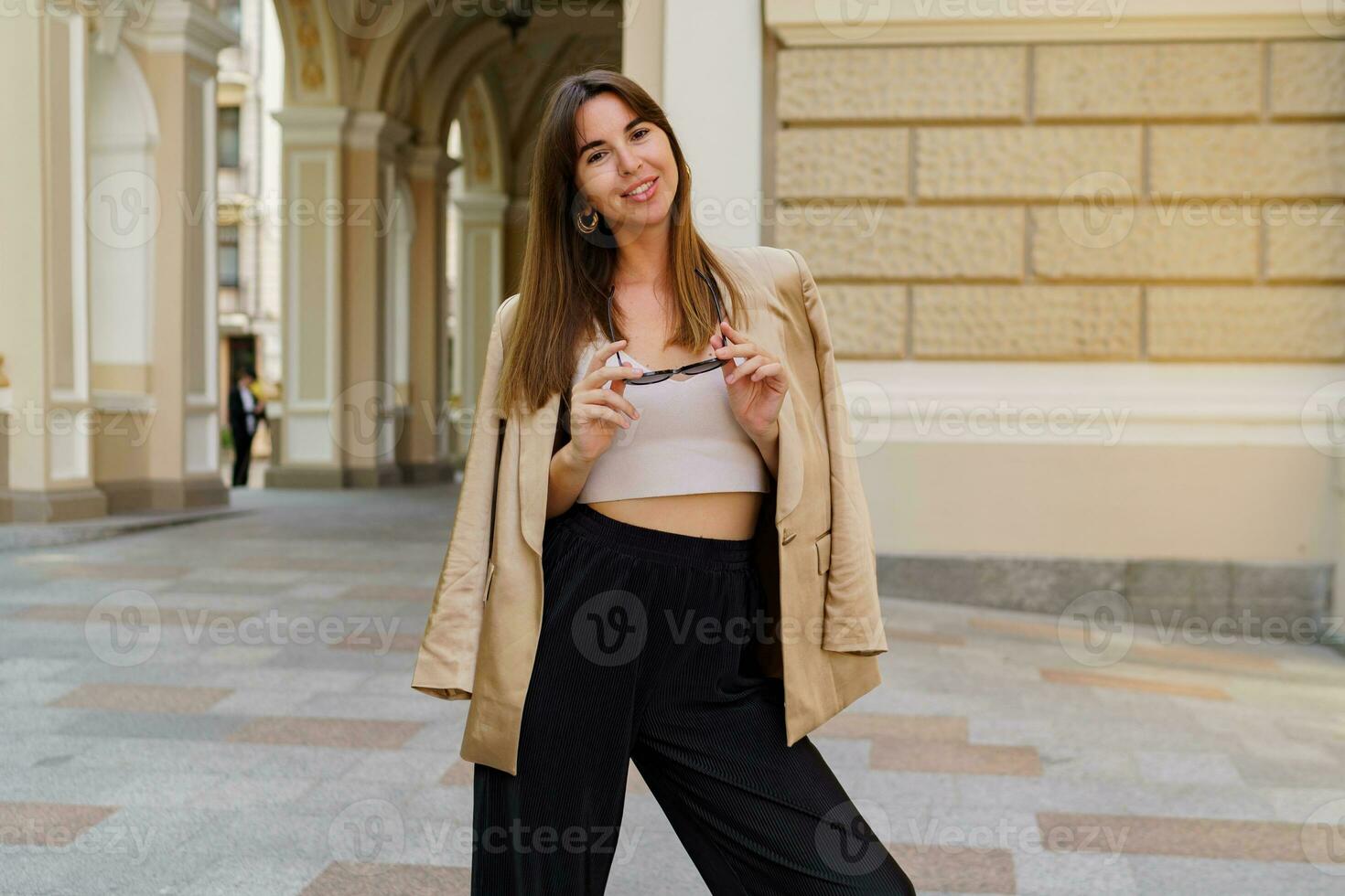 elegante morena mujer en dorado lujo chaqueta posando al aire libre en hermosa europeo calle. verano elegancia moda. foto