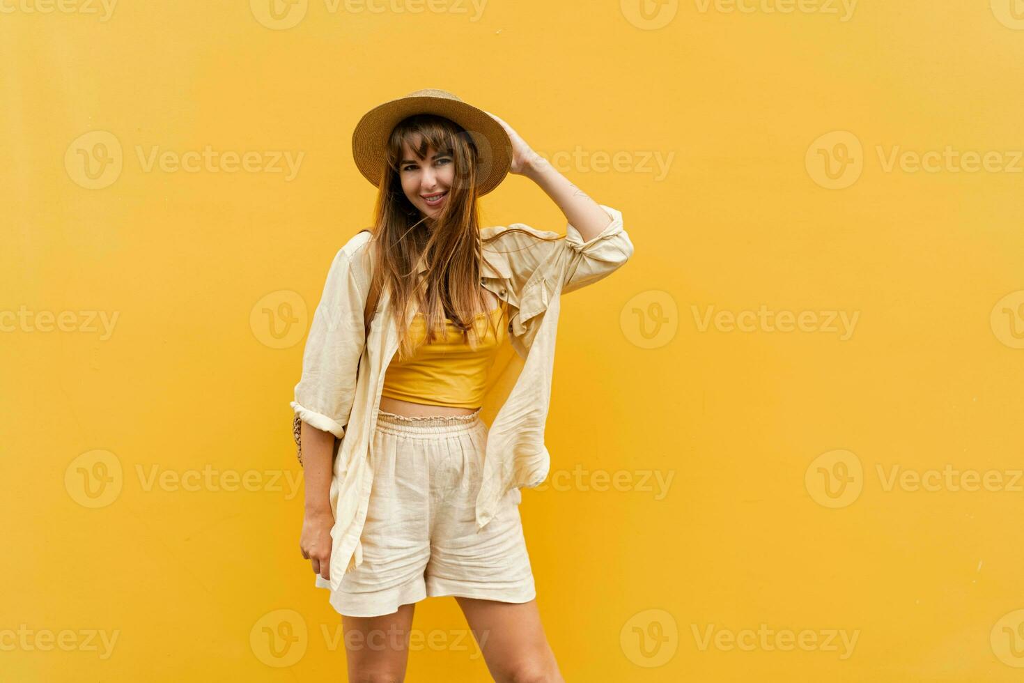 Smiling  carefree woman in straw hat and trendy summer linen  outfit  and posing on yellow background.  Vacation  and travel concept. photo