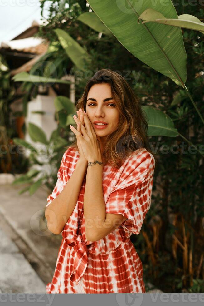 Fashion image of sexy tanned woman in  summer outfit posing in modern hotel in Thailand.  Palm trees on background. photo