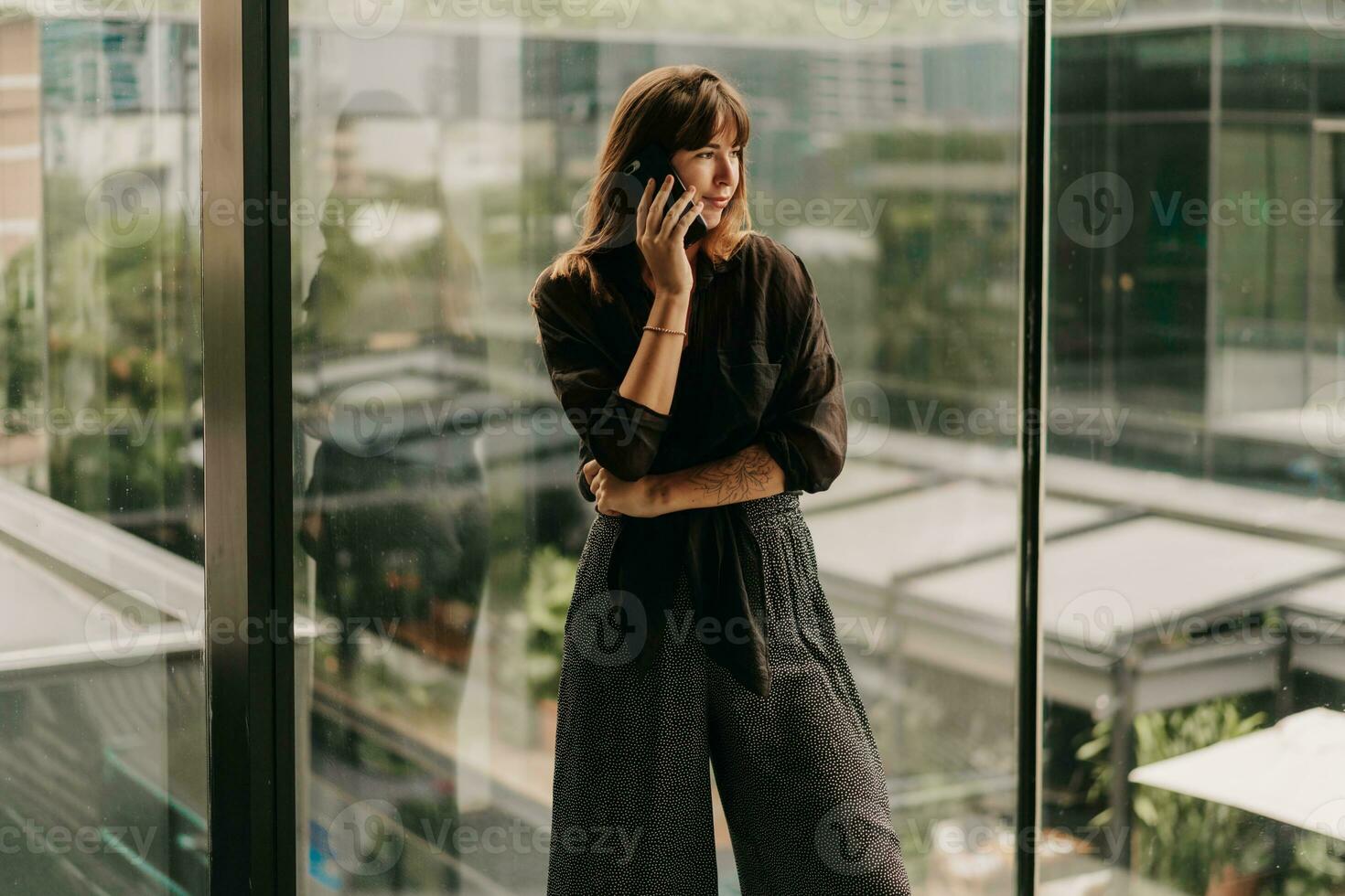 elegante negocio mujer en de moda casual atuendo hablando por móvil teléfono durante trabajo día en moderno negocio centro. foto