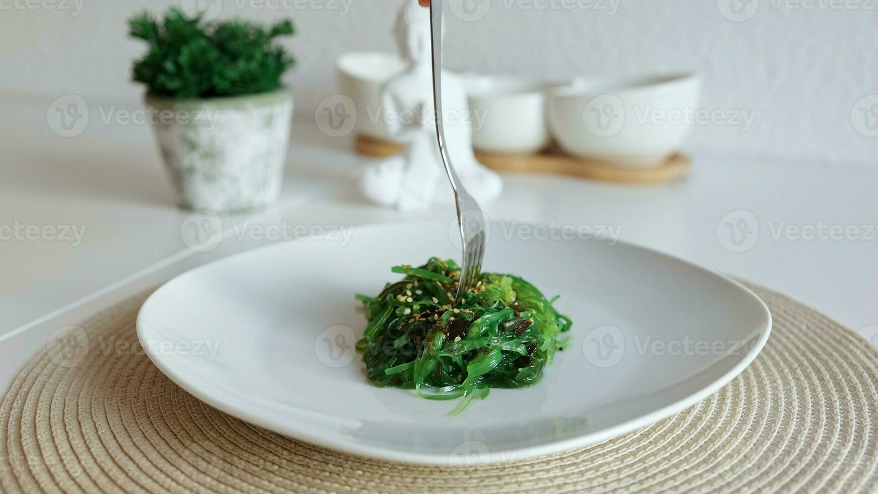 Japanese Wakame seaweed salad with sesame on white plate.  Woman eating tasty seaweed salad  with fork photo