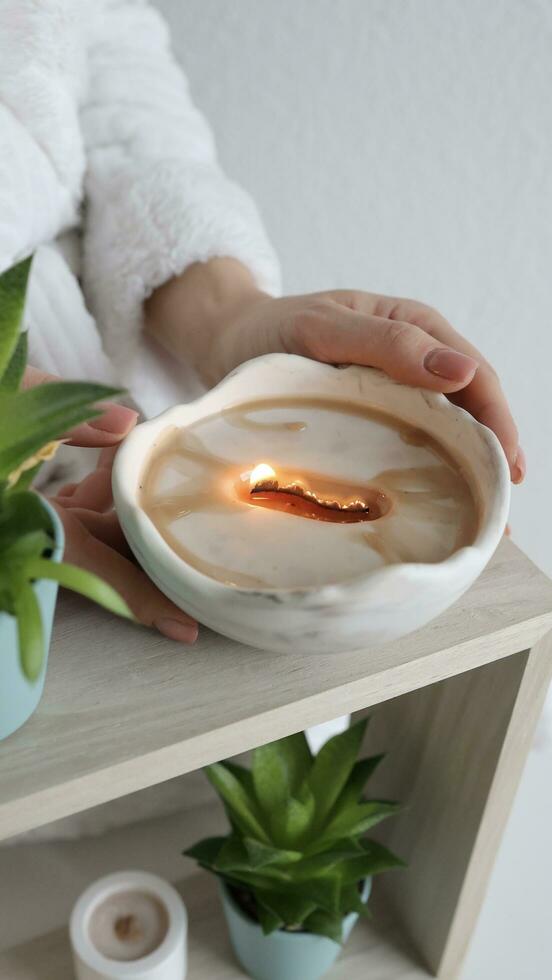 Female hands holding scented candle, top view. Burning white wax candle on a table. Home decor photo