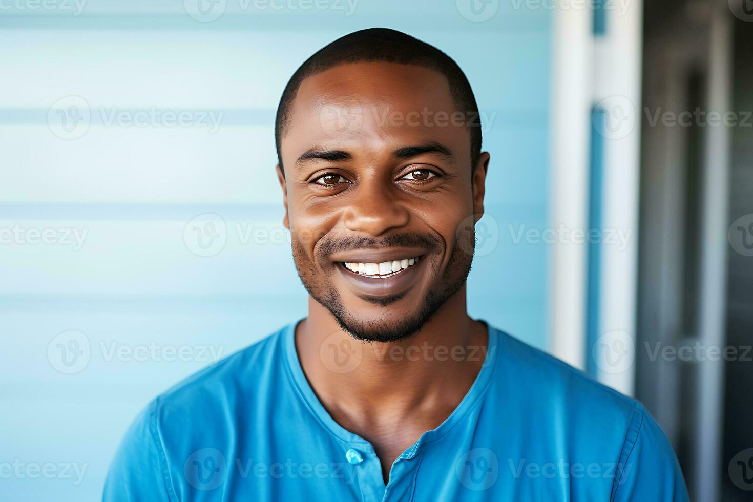 A young African-American man in a blue t-shirt stands in front of a blue wall, looks at the camera and smiles. AI Generative photo