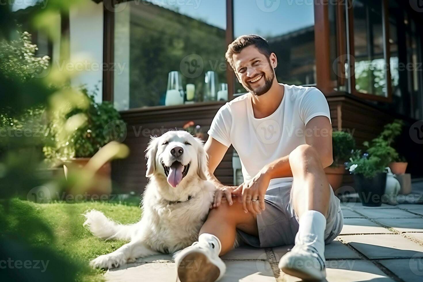 A man in a white T-shirt and shorts poses with his dog in the courtyard of the house on a sunny day. Man looking at camera and smiling. AI Generative photo