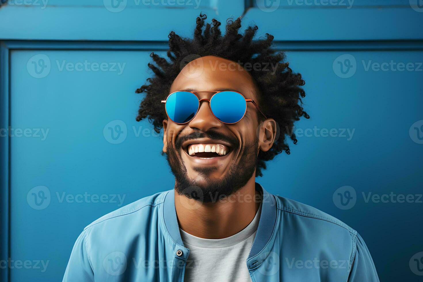 Young African American man in a blue jacket and blue sunglasses laughs and poses on a blue background. AI Generative photo