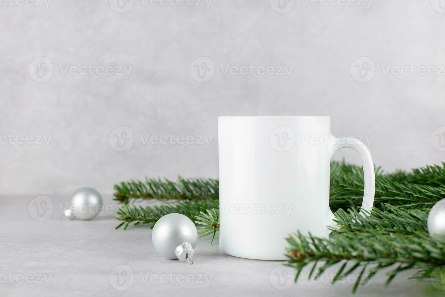 Blank white mug mockup with christmas tree branches and silver balls on light concrete stone background. Holiday composition. Side view. Copy space. photo