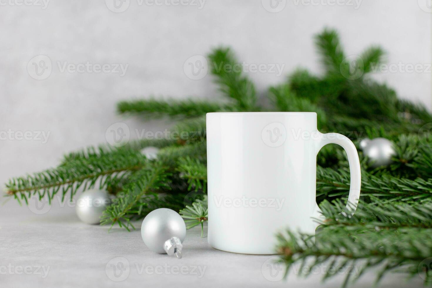 Blank white mug mockup with christmas tree branches and silver balls on light concrete stone background. Holiday composition. Side view. Copy space. photo