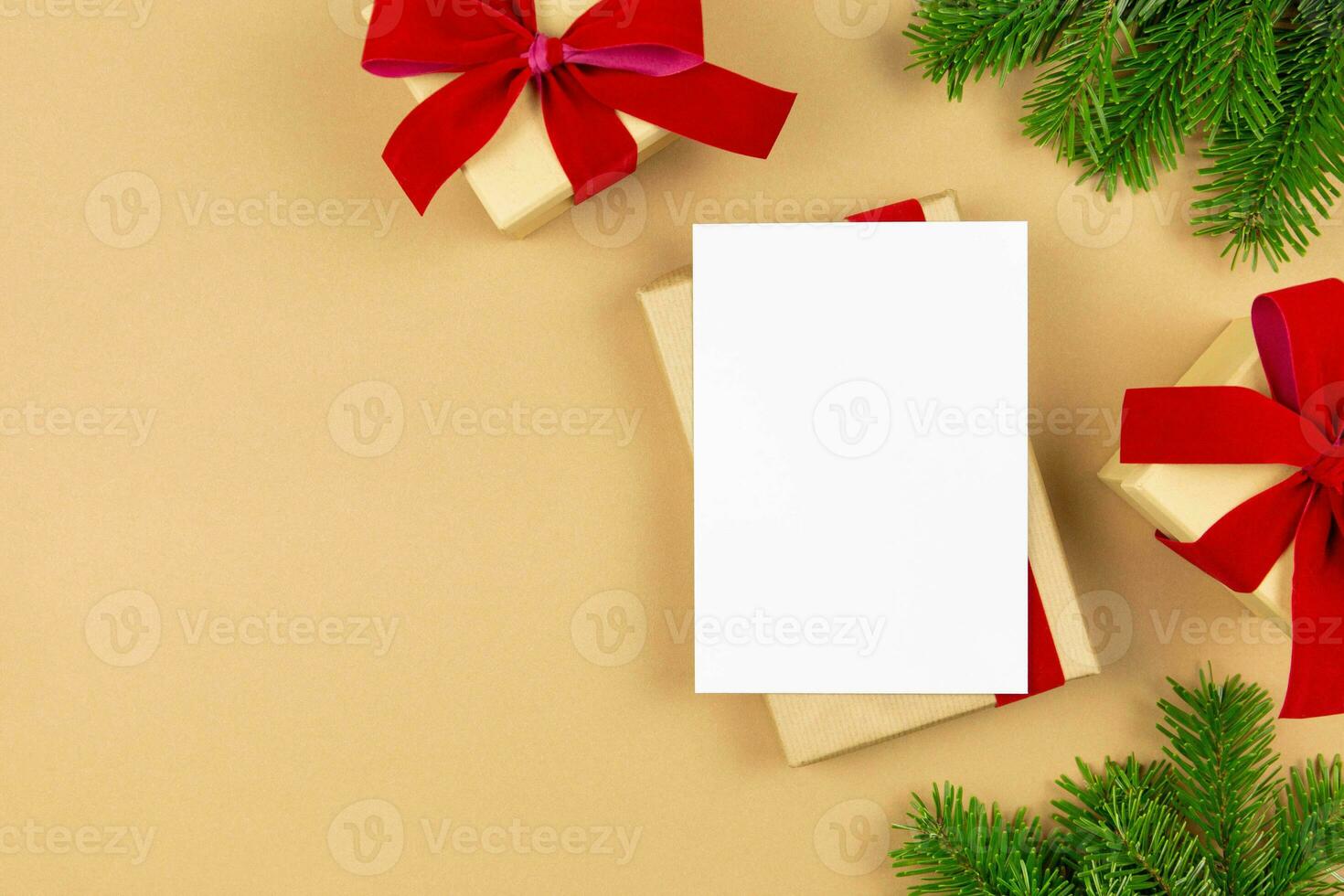 Christmas greeting card mockup and wrapped gift boxes with red ribbon and christmas tree branches on paper background. Festive flat lay styled template composition. Top view. photo