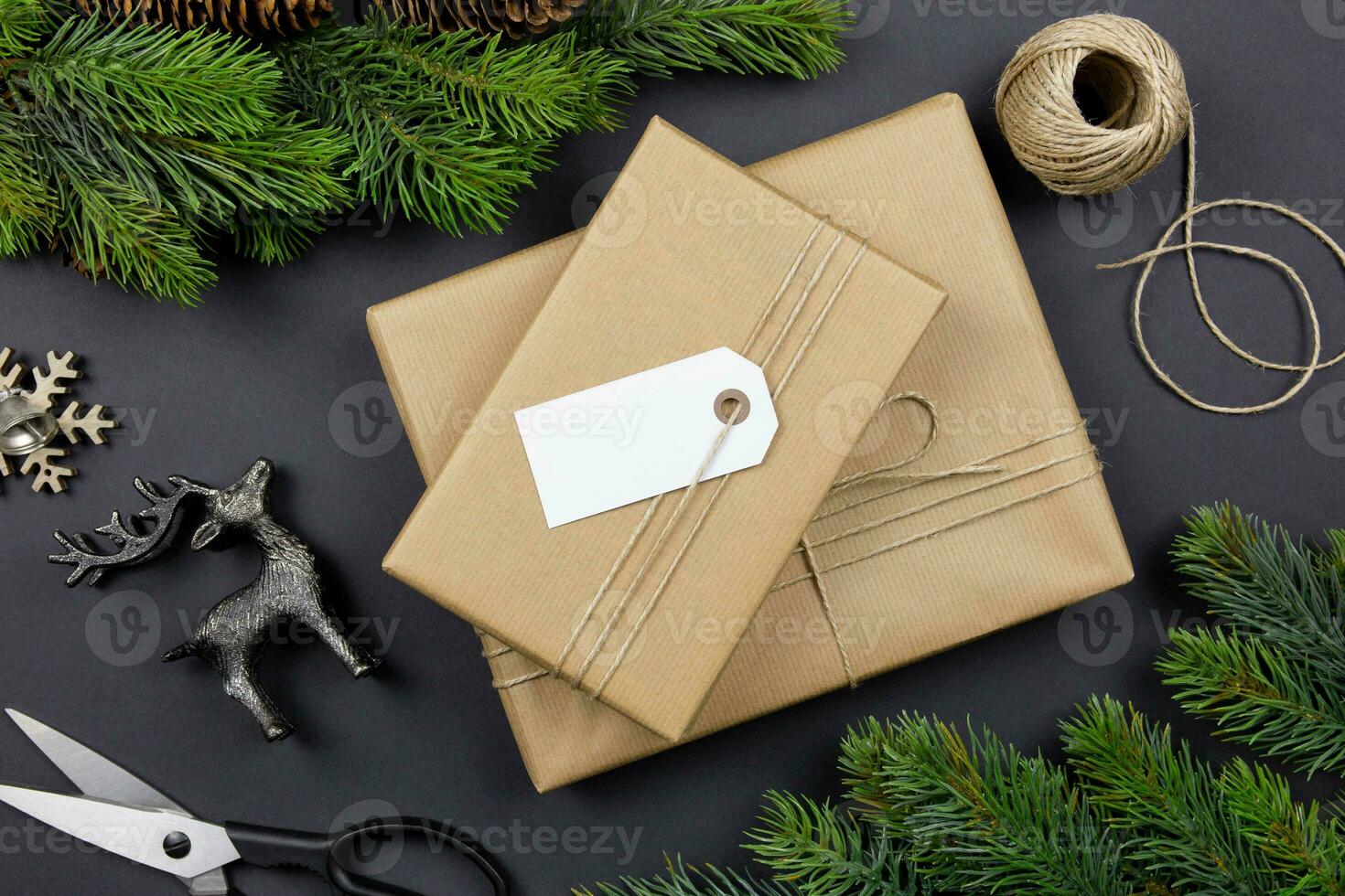 Christmas handmade gift box with label tag mockup, pine cones, fir tree branches and decoration on dark background. Festive styled composition. Top view. photo