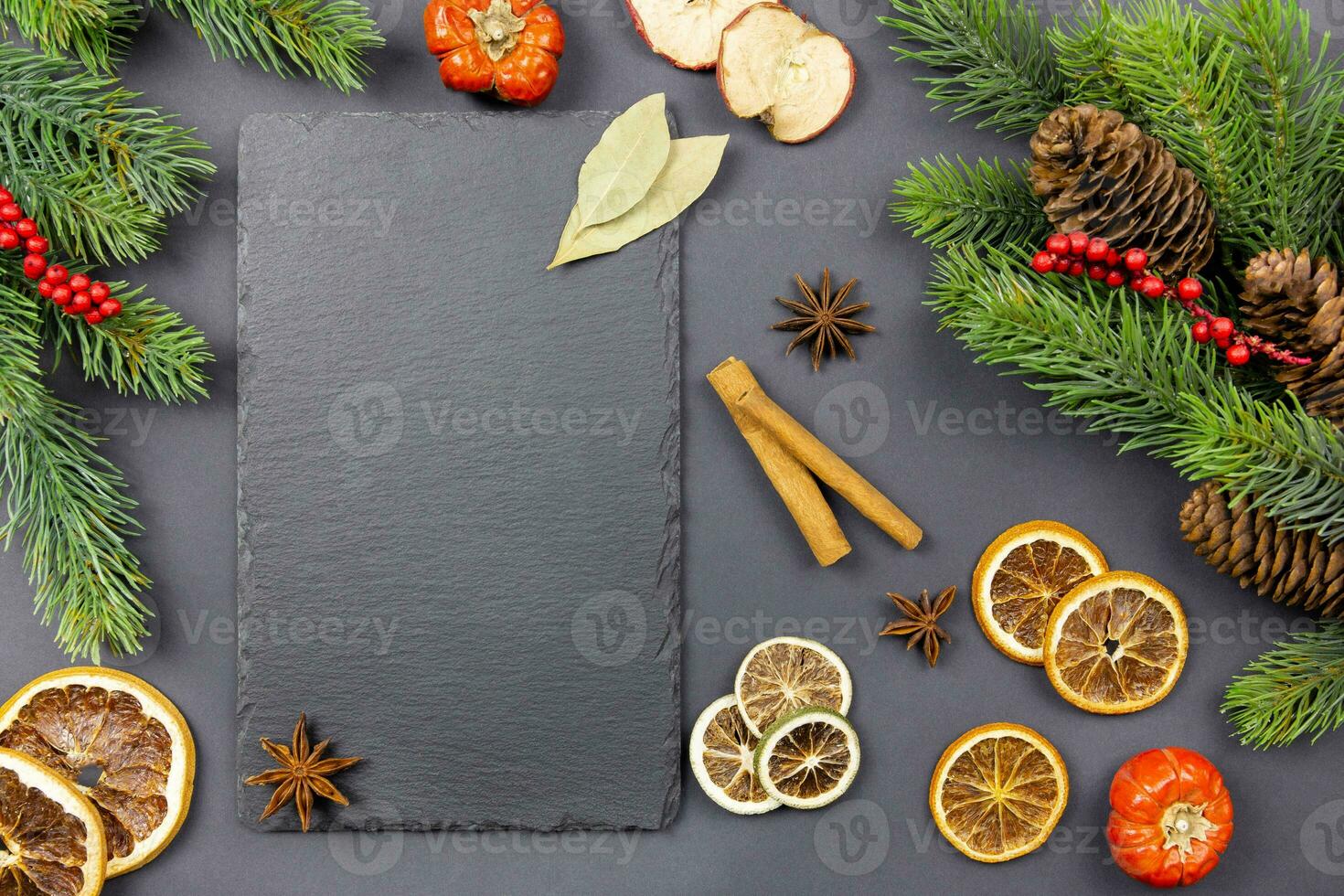Winter dried fruits and culinary spice background mockup with christmas tree branches and pine cones on dark background with a black slate chalkboard for your text. Top view. Copy space. photo