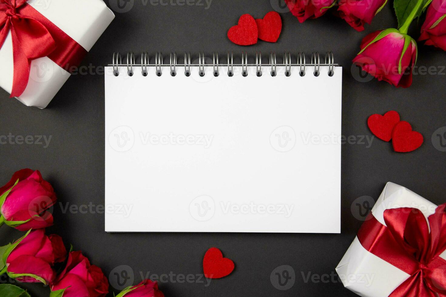 Paper spiral notebook mockup and gift boxes with red ribbon, hearts, roses on dark background. Valentines, mothers, womens day, anniversary and birthday greeting flat lay. Top view. Copy space. photo