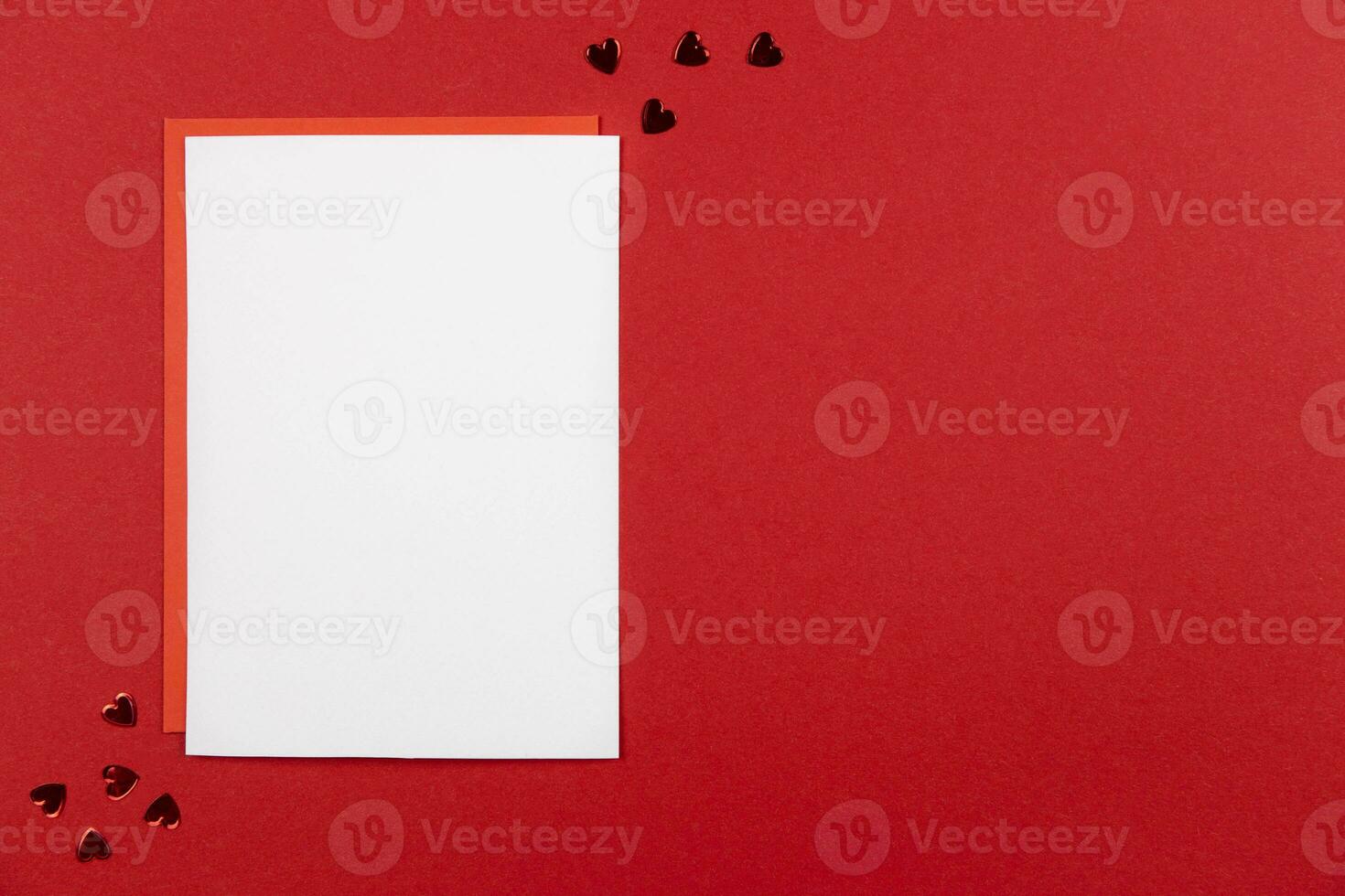 Blank greeting card mockup and envelope on red background with hearts confetti. Valentines, mothers, womens day or wedding flat lay composition. Top view. Copy space. photo