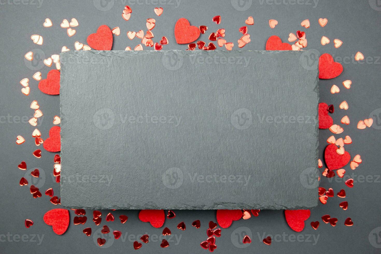 Red hearts confetti and black slate chalkboard mockup on dark background. Valentines, mothers, womens day, 8 march, birhday or wedding flat lay concept. Top view with copy space for your design. photo