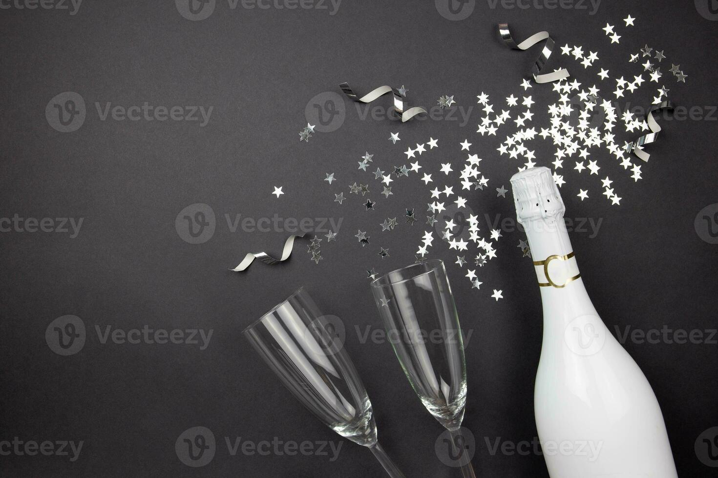Champagne bottle, wine glasses and confetti on dark background. Flat lay composition of celebration. Top view. Copy space. photo