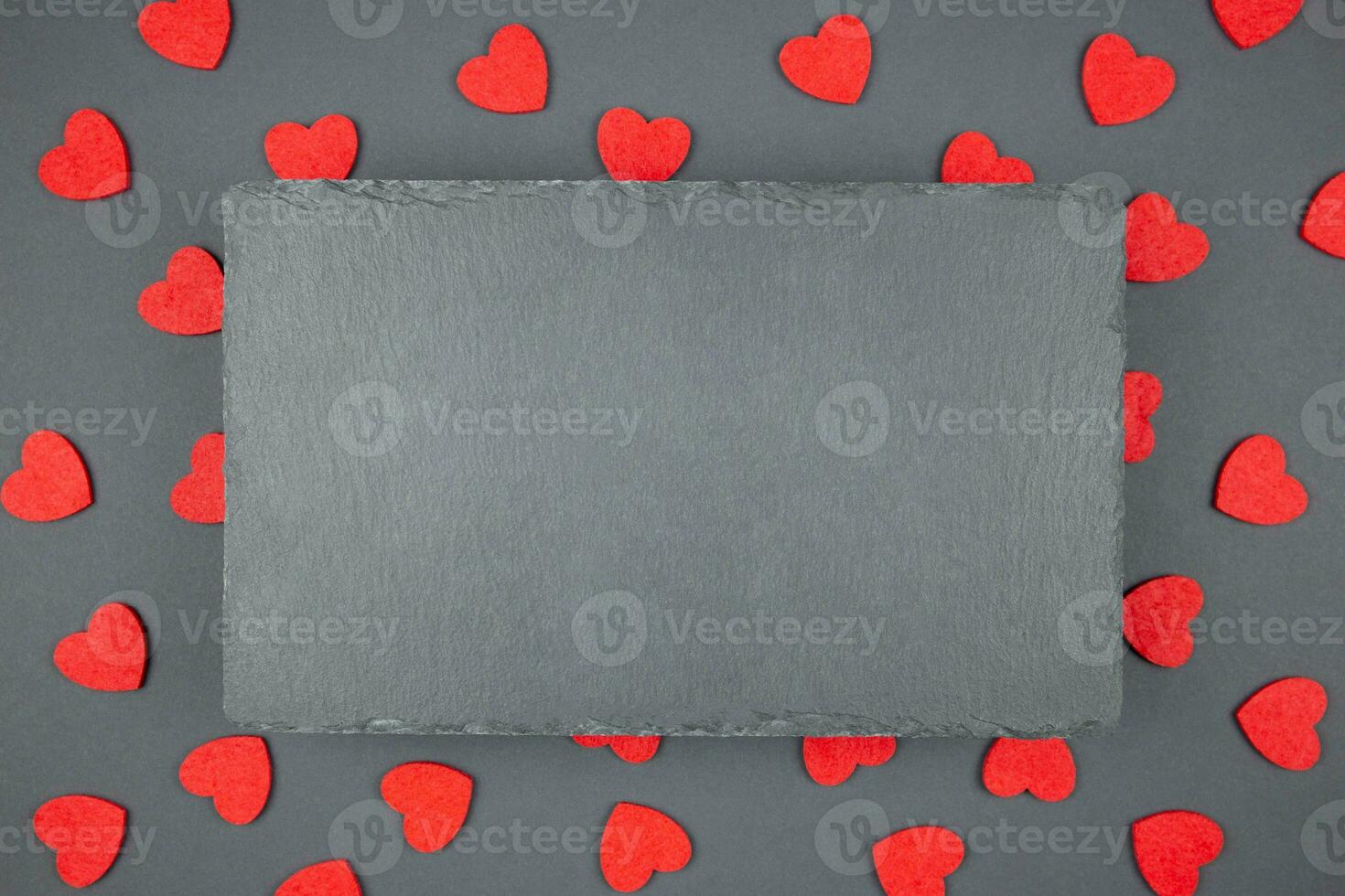Red hearts confetti and black slate chalkboard mockup on dark background. Valentines, mothers, womens day, 8 march, birhday or wedding flat lay concept. Top view with copy space for your design. photo