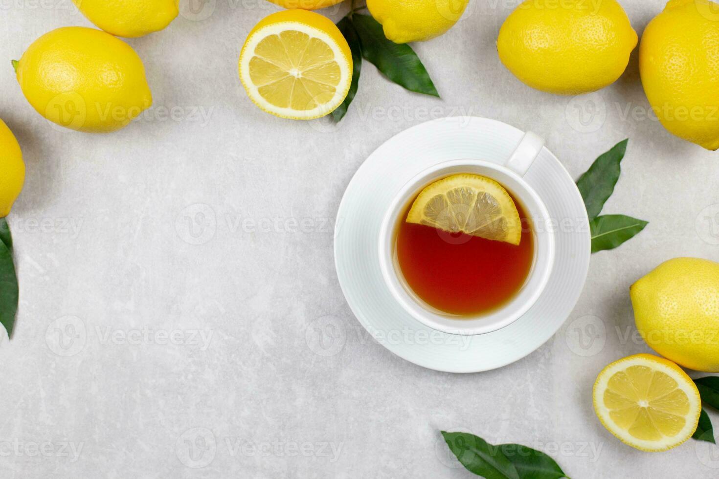 Cup of tea with fresh lemons and leaves on light gray concrete background. Hot healthy beverage. Immune defence, vitamin c. Top view. Copy space. photo