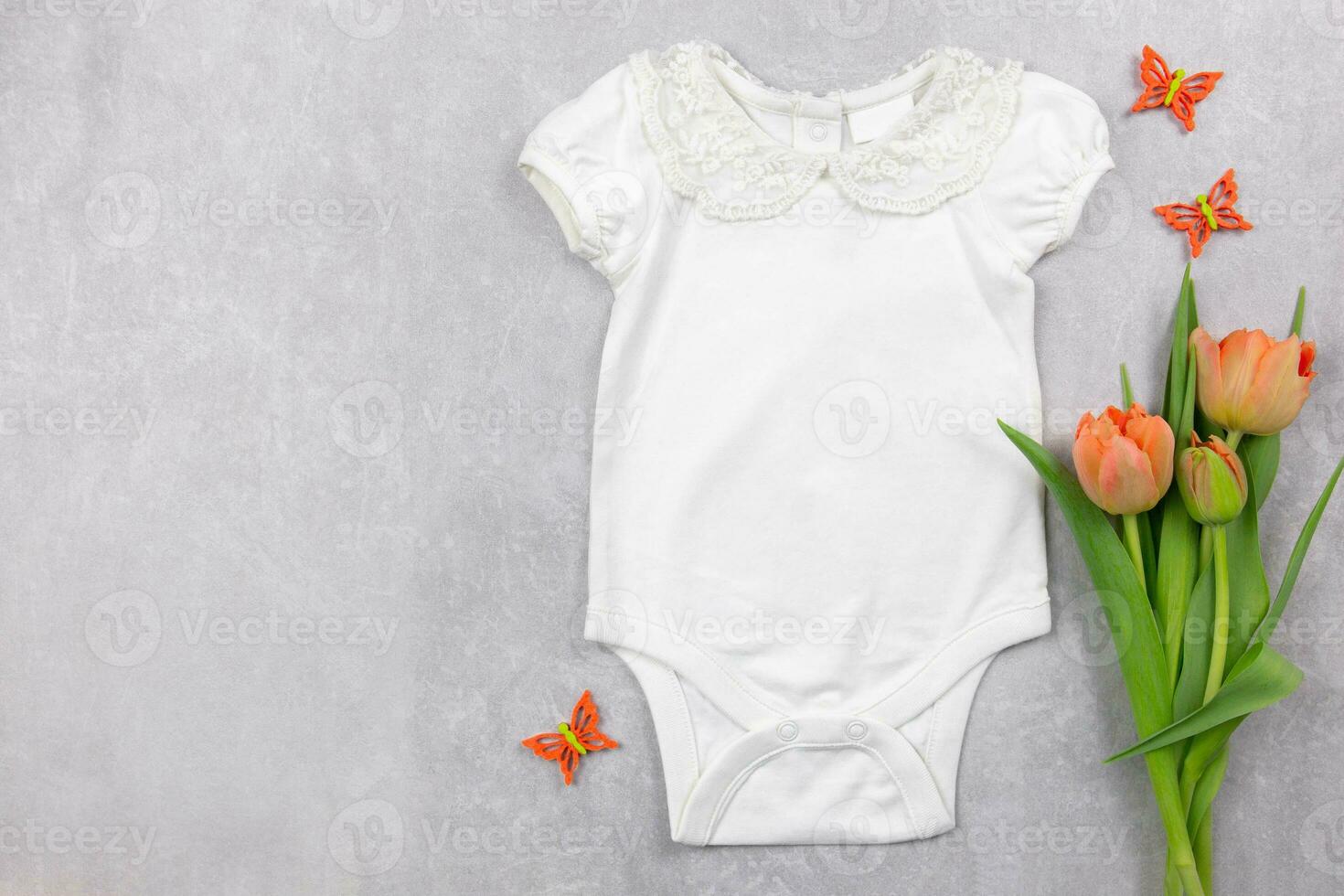 White baby girl bodysuit mockup flat lay with orange tulips flowers and butterflies decoration on the gray concrete background. Design onesie template, print presentation mock up. Top view. photo