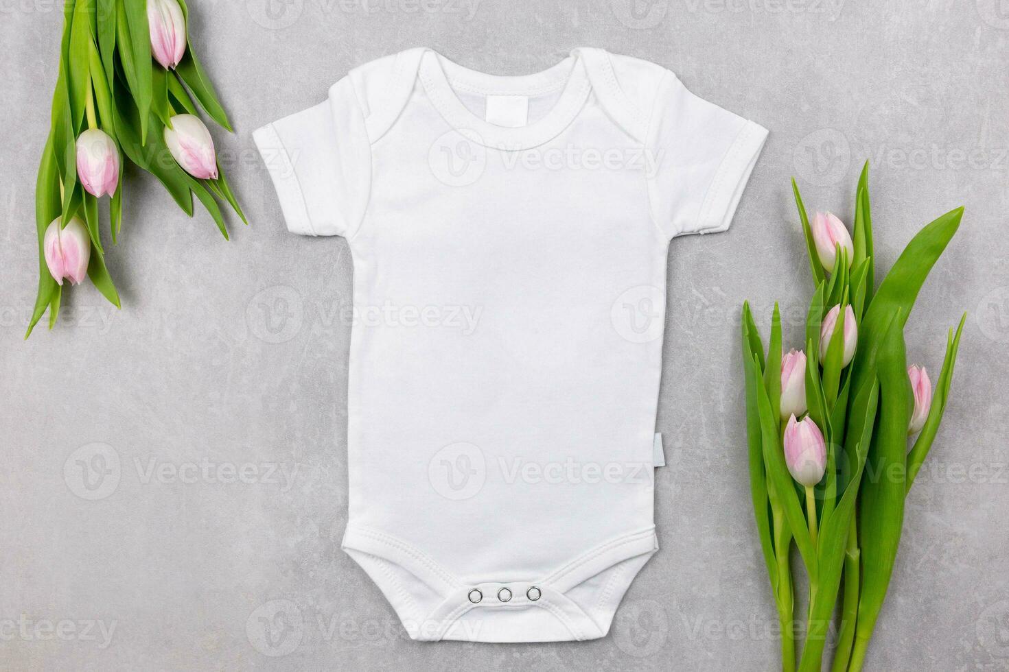 White baby girl or boy bodysuit mockup flat lay with pink tulips flowers on the gray concrete background. Design onesie template, print presentation mock up. Top view. photo