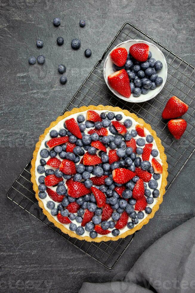 Delicious blueberry and strawberry tart with whipped cream and mascarpone on a dark stone background. Top view. photo