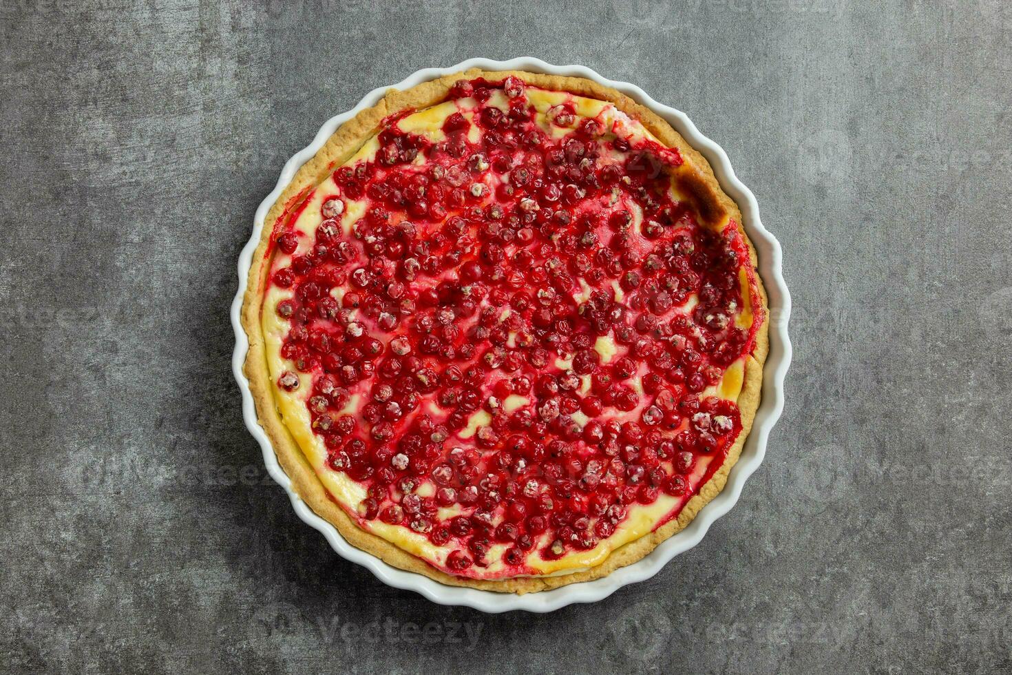 Redcurrant cheesecake, tart with fresh berries in a white baking dish on dark gray background. Top view. photo