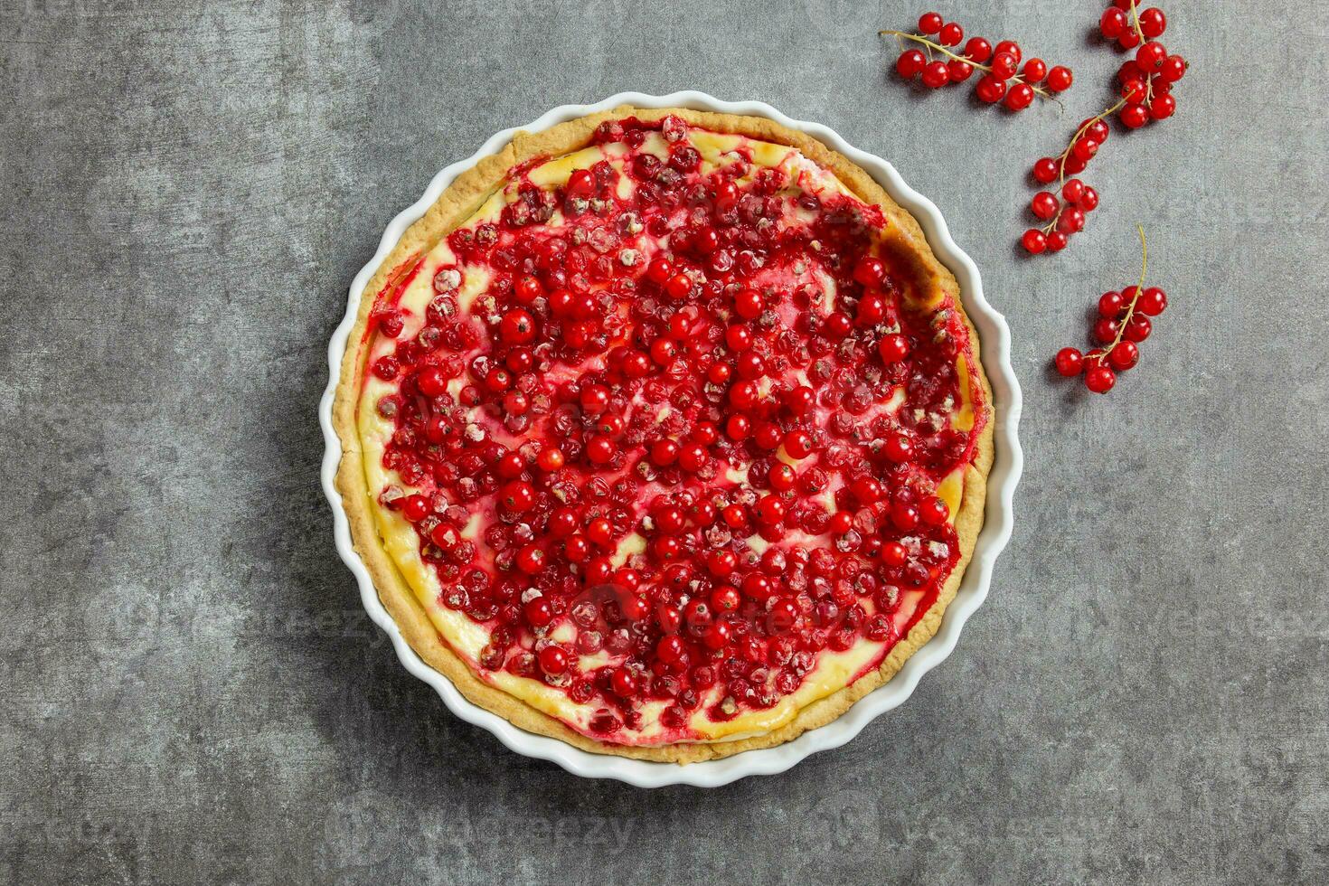 Redcurrant cheesecake, tart with fresh berries in a white baking dish on dark gray background. Top view. photo