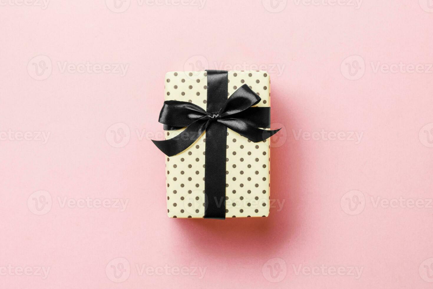 Gift box with black bow for Christmas or New Year day on pink background, top view with copy space photo