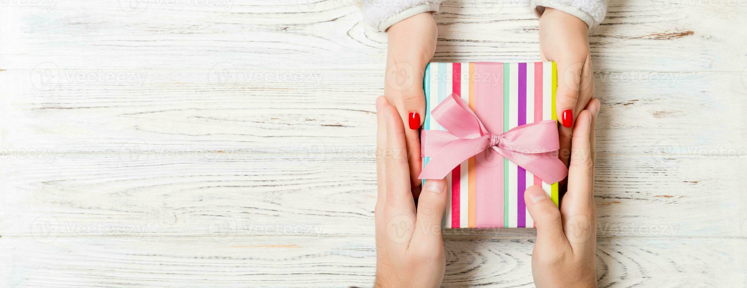 Top view of two people sharing a present on wooden background. Holiday and surprise concept. Copy space photo